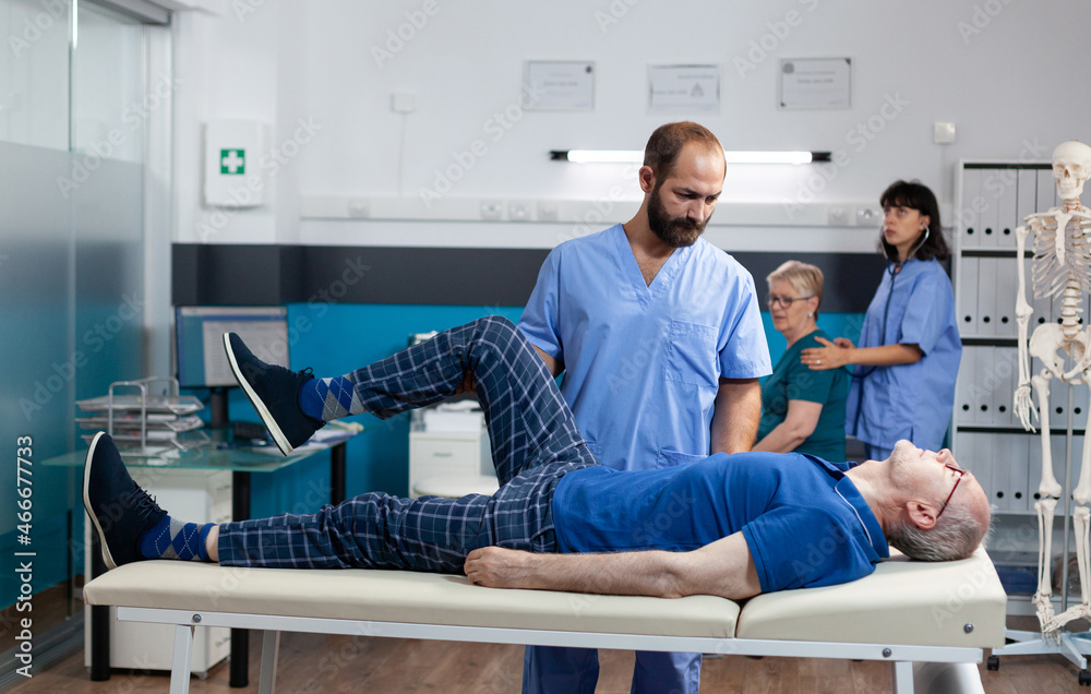 Obraz premium Man with leg muscle injury receiving orthopedic massage for physiotherapy. Nurse helping retired patient with knee pain, relieving pressure for physical recovery and kinetotherapy.