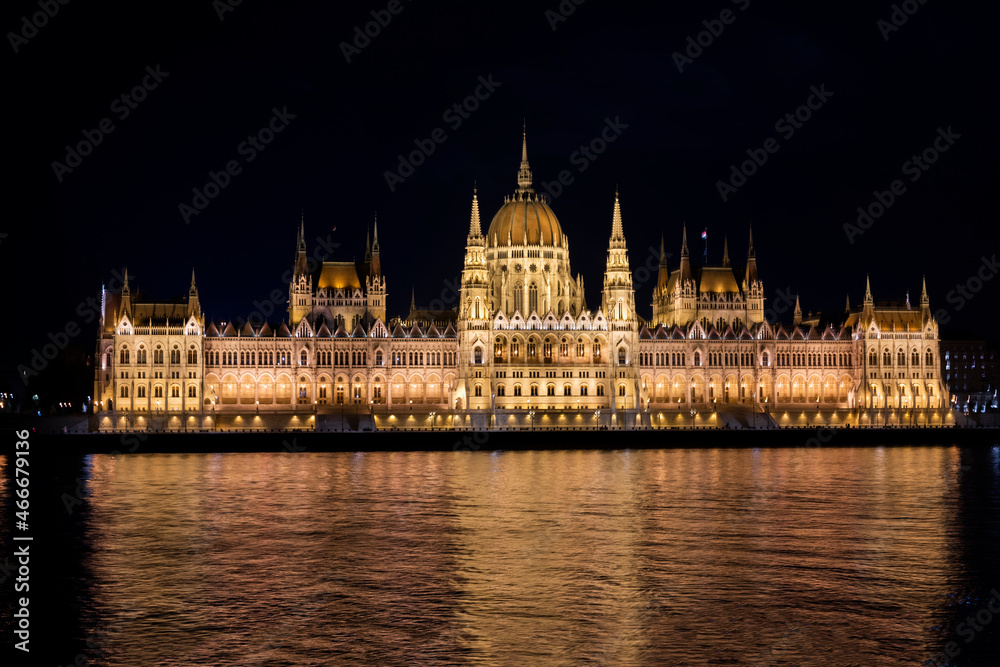 view of the facade of the building of the parliament of budapest hungary at sunset at night with lights on the banks of the Danube river