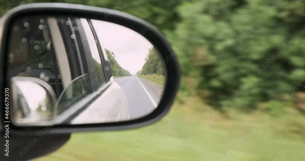 Rearview mirror of driving car, close-up. In rearview mirror reflection moving road lane markings receding into distance, white automobile. Summer car travel, rent concept. Green trees on road sides Rearview mirror of driving car, close-up. In rearview mirror reflection moving road lane markings receding into distance, white automobile. Summer car travel, rent concept. Green trees on road sides
