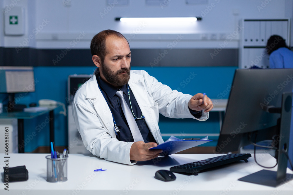 Doctor using computer and checkup files for healthcare work at night. Specialist analyzing information on monitor for prescription medicine and medical advice, working late at office.