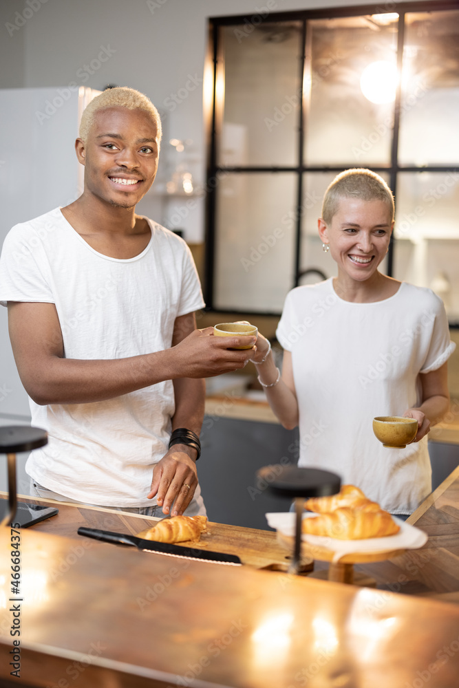 Multiracial couple drinking and toasting drink at home kitchen. Concept of relationship. Idea of modern domestic lifestyle. Black man and european girl spending time together in modern flat Multiracial couple drinking and toasting drink at home kitchen. Concept of relationship. Idea of modern domestic lifestyle. Black man and european girl spending time together in modern flat