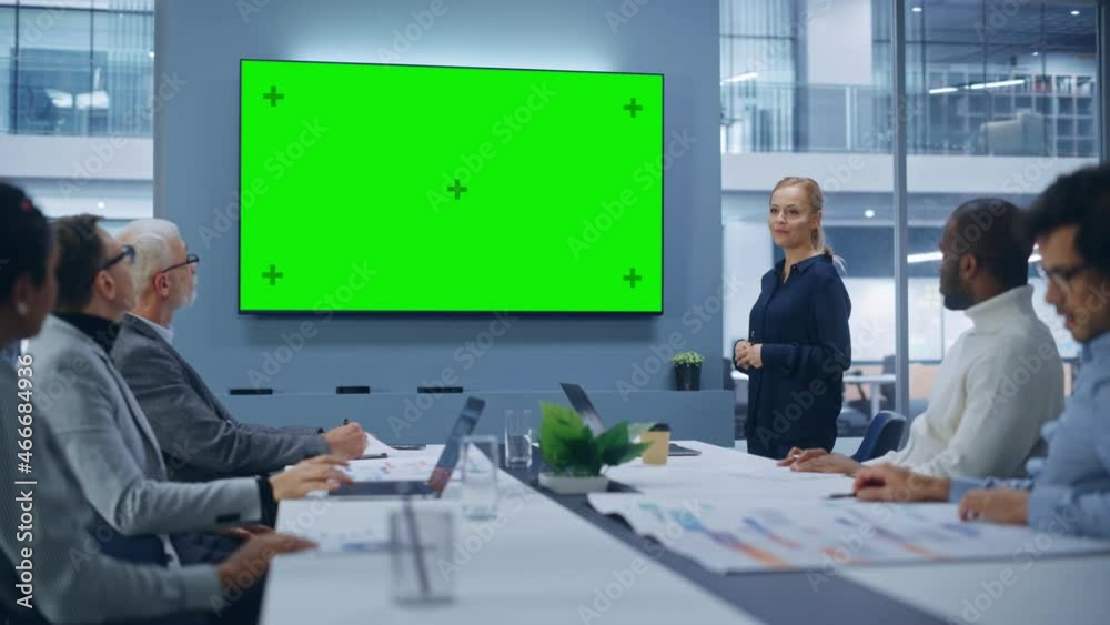 Office Conference Room Meeting Presentation: Beautiful Businesswoman Talks, Uses Green Screen Chroma Key Wall TV. Digital Entrepreneur Presents e-Commerce Product to Group of Multi-Ethnic Investors