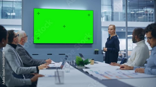 Office Conference Room Meeting Presentation: Beautiful Businesswoman Talks, Uses Green Screen Chroma Key Wall TV. Digital Entrepreneur Presents e-Commerce Product to Group of Multi-Ethnic Investors photo