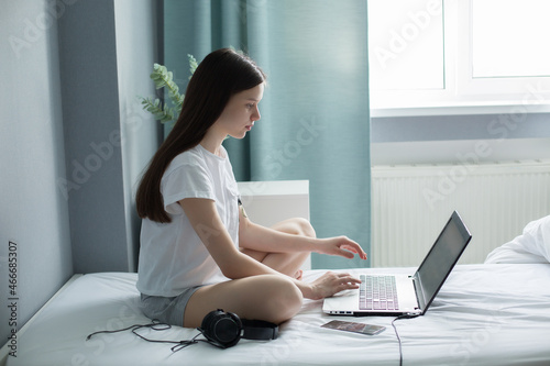 teen school girl student virtual distance learning online digital class looking at laptop sitting on bed at home.