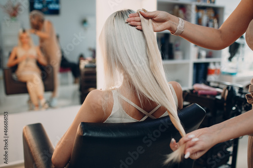 Hairdresser female making hair extensions to young woman with blonde hair in beauty salon. Professional hair extension salon photo