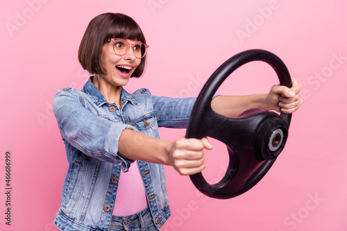 Portrait of attractive cheerful impressed girl driving steering wheel having fun isolated over pink pastel color background