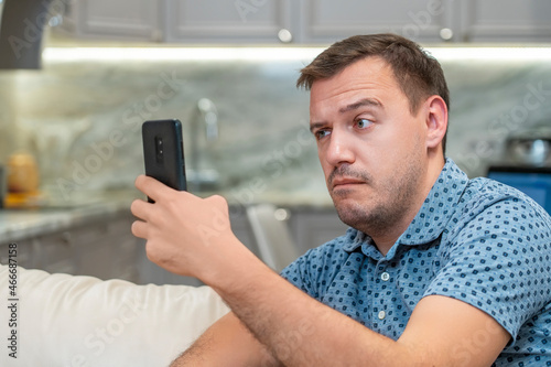 Surprised millennial man with shoke look at smartphone screen at modern living room. Manager cringe and looking at phone screen with confuse. Confused man thinking of problem solution stuck with task