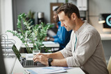 Side view portrait of smiling adult man using laptop while enjoying work in office, copy space