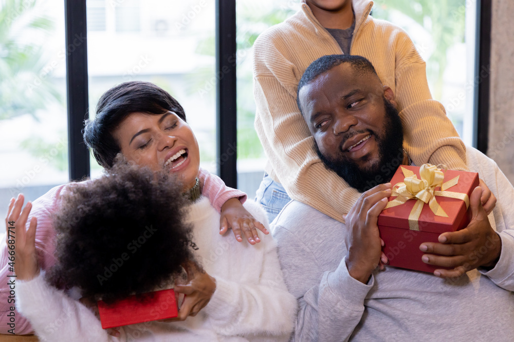 Cheerful african american daughter with curly hair closing parent eyes while presenting christmas and thanksgiving gift at home