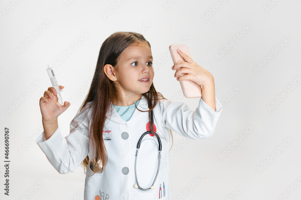 Close-up portrait of cute little girl, child in image of doctor wearing white lab coat with stethoscope isolated on white studio background Close-up portrait of cute little girl, child in image of doctor wearing white lab coat with stethoscope isolated on white studio background