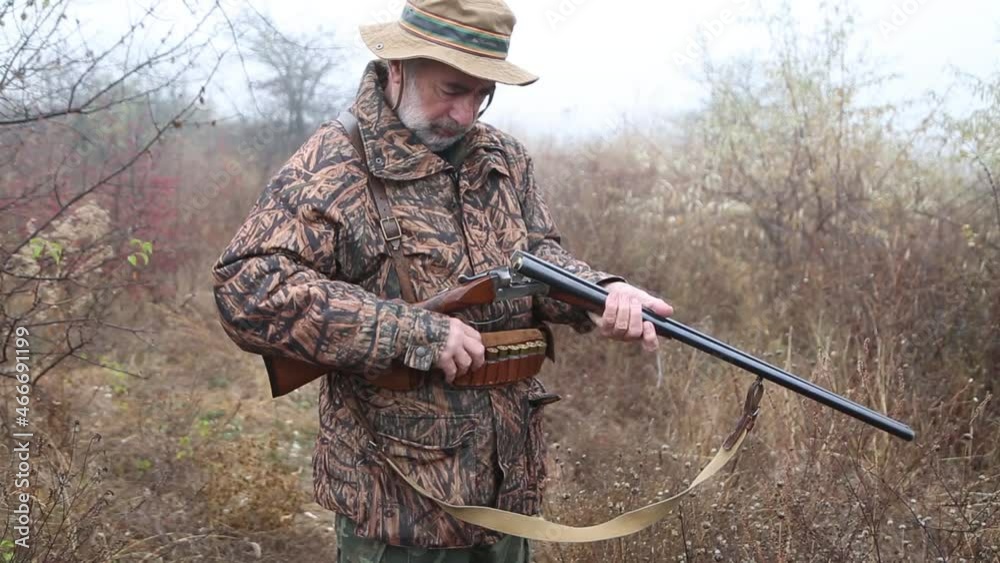 hunter man with gray beard in hunter suit load cartridges in a double-barreled rifle and makes aiming wiring hunter man with gray beard in hunter suit load cartridges in a double-barreled rifle and makes aiming wiring