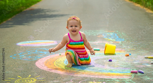 The child draws with chalk on the asphalt. Selective focus.