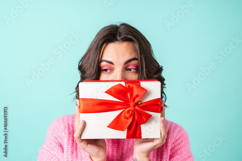 Cozy portrait of a young woman in a pink knitted sweater and with bright makeup on a turquoise background with a gift box with a red bow