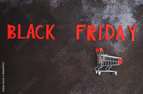 Black Friday concept. Inscription "black friday", mini shopping cart on black background. Copy space, top view, flat lay. Creative holiday flyer. Online sale and discounts