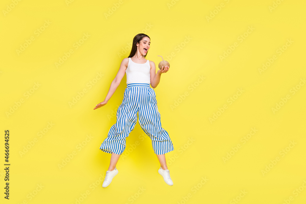 Full length body size view of charming cheerful girl jumping drinking juice isolated over bright yellow color background Full length body size view of charming cheerful girl jumping drinking juice isolated over bright yellow color background