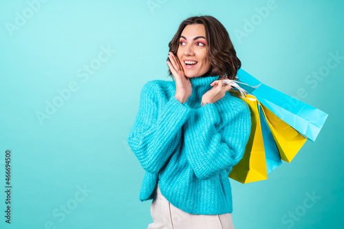Cozy portrait of a young woman in a knitted blue sweater and bright pink makeup on a turquoise background holding shopping bags