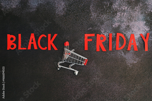 Black Friday concept. Inscription "black friday", mini shopping cart on black background. Copy space, top view, flat lay. Creative holiday flyer. Online sale and discounts