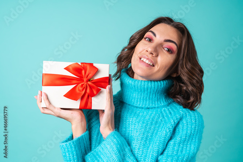 Cozy portrait of a young woman in a knitted blue sweater and bright pink makeup holding a gift box