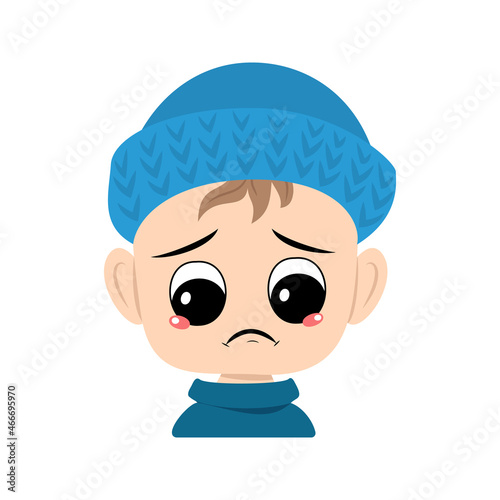 Boy with crying and tears emotion, sad face, depressive eyes in blue knitted hat. Cute kid with melancholy expression in autumnal or winter headdress. Head of adorable toddler