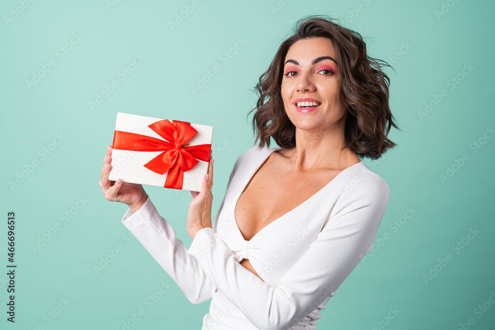 Young woman in a white evening dress on a light green background with bright pink makeup holding a gift box Young woman in a white evening dress on a light green background with bright pink makeup holding a gift box