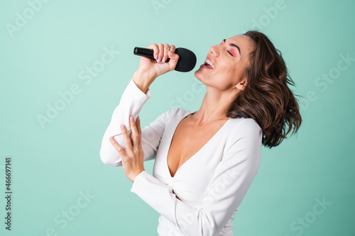 Young woman in a white evening dress on a light green background with bright pink makeup holds a microphone, sings karaoke