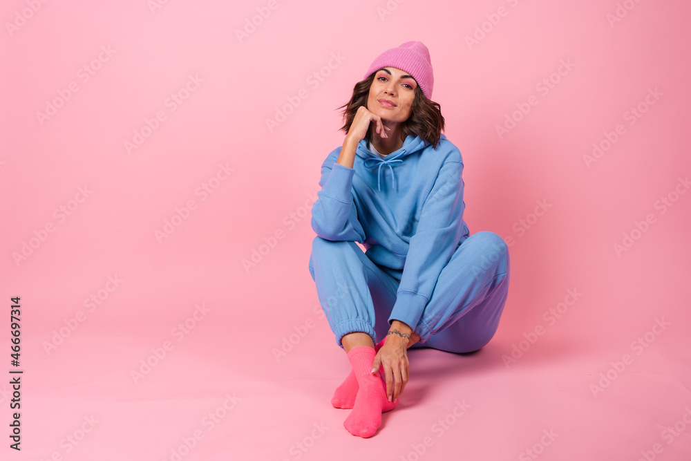 Young woman in a cozy suit on a fleece, a hoodie and pants, on a pink background, a knitted hat on her head Young woman in a cozy suit on a fleece, a hoodie and pants, on a pink background, a knitted hat on her head