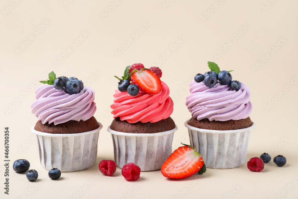 Different delicious cupcakes with cream and berries on beige background Different delicious cupcakes with cream and berries on beige background