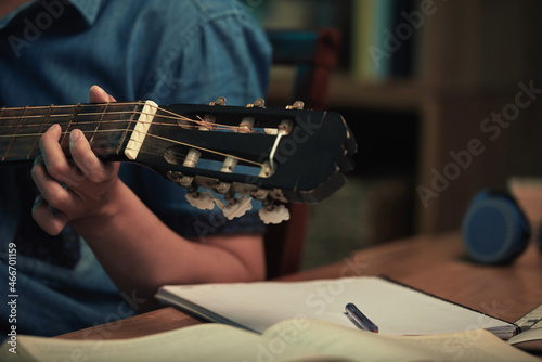 Close-up of unrecognizable man sitting at table and learning to play guitar using manual at night