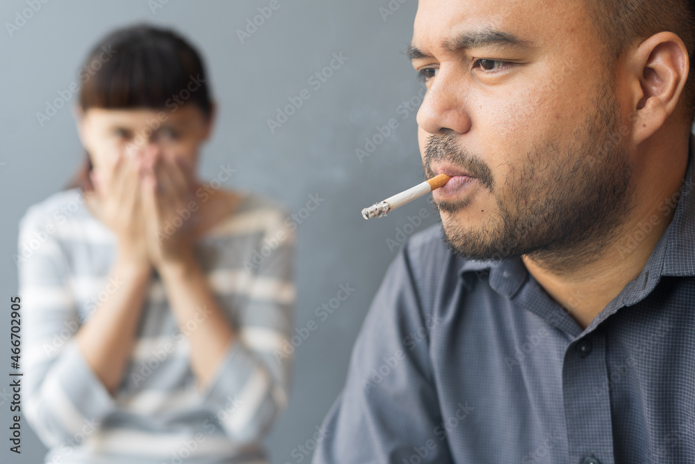 Husband smoking cigarette and wife choking of smoke. Man smoking