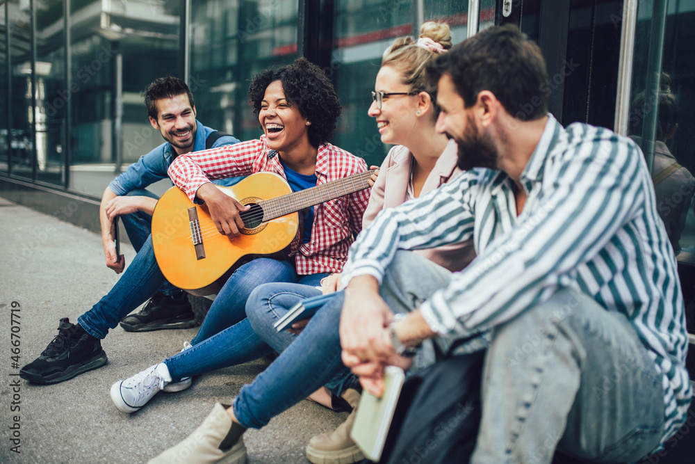 Group of young friends hangout in city.They are sitting,singing and playing guitar.