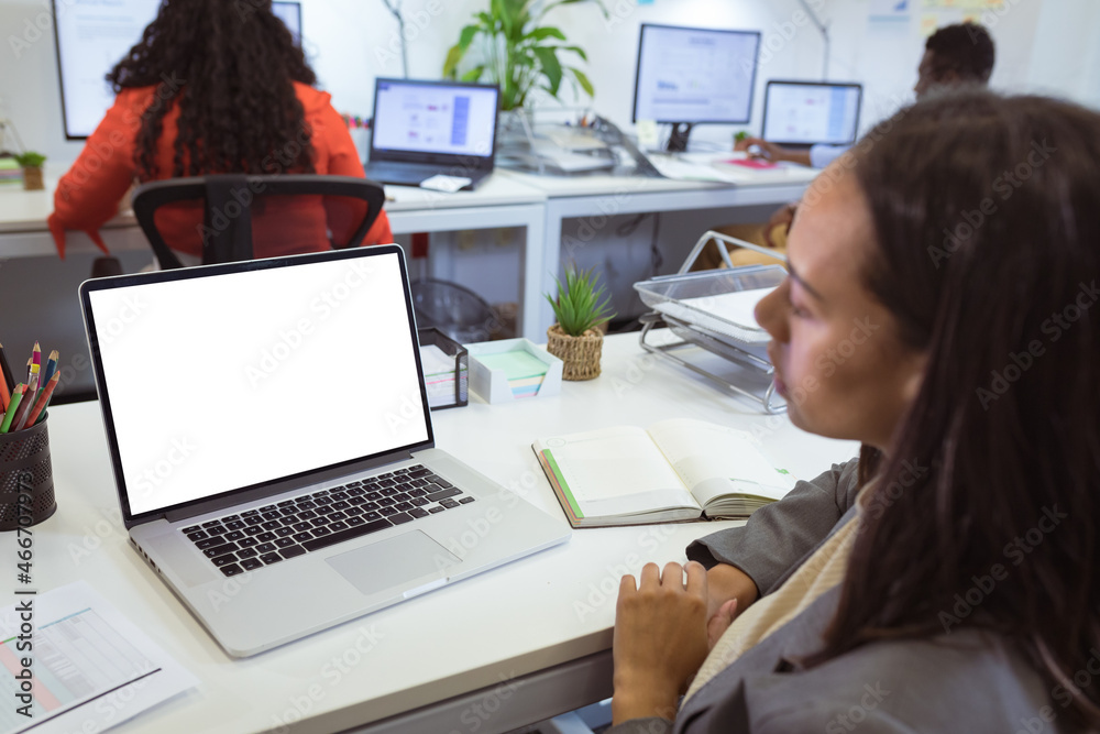 Biracial businesswoman sitting at desk using laptop with copy space in modern office Biracial businesswoman sitting at desk using laptop with copy space in modern office