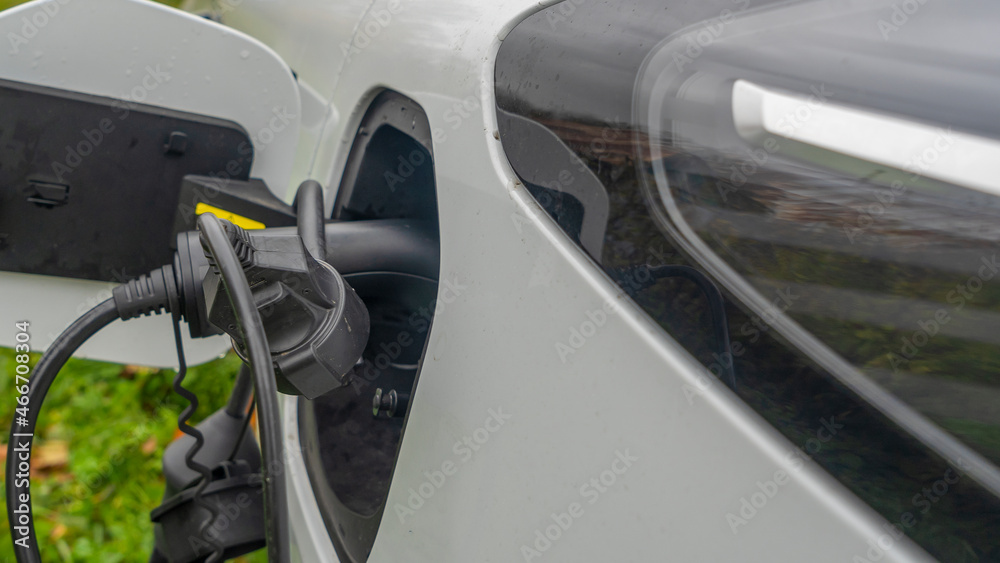 Close-up view of power supply plugged into an electric car being charged. White electric car charging.