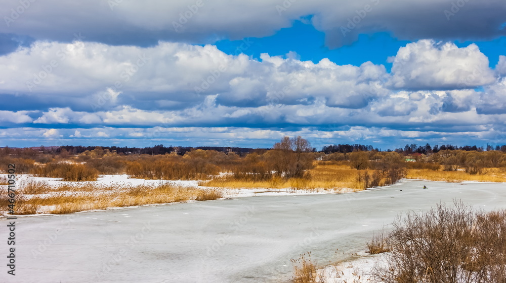 Spring landscape with frozen river, trees, shrubs, blue sky with clouds Spring landscape with frozen river, trees, shrubs, blue sky with clouds