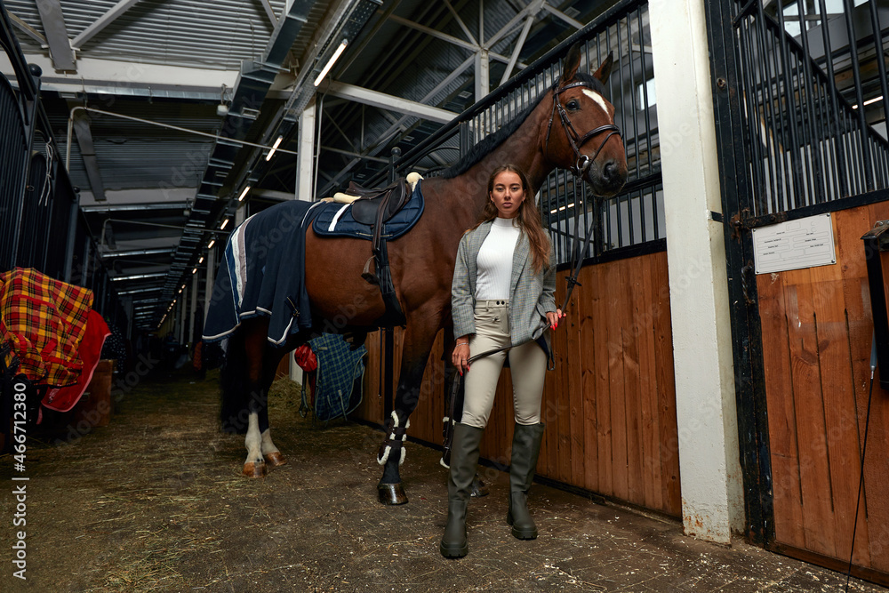 Portrait of smiling female jockey standing by horse in stable Portrait of smiling female jockey standing by horse in stable