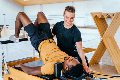 Εκτύπωση καμβά African american man doing pilates on reformer bed with instructor in modern interior pilates studio