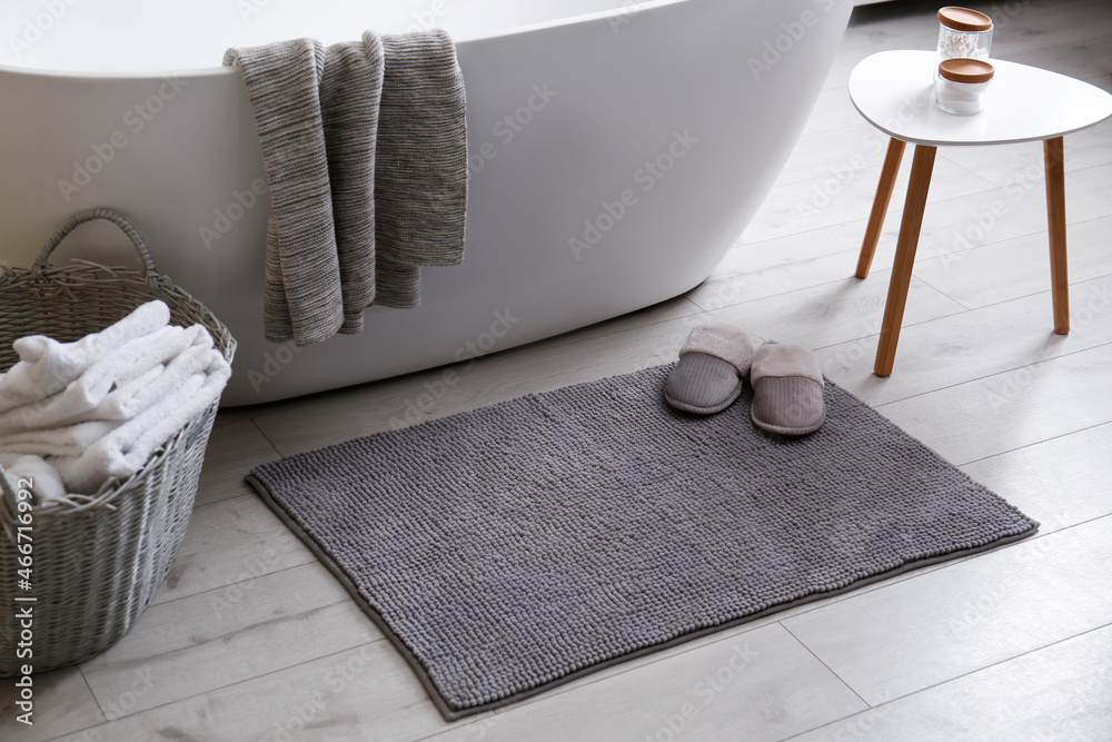 Soft grey mat with slippers on floor near tub in bathroom. Interior design - obrazy, fototapety, plakaty 