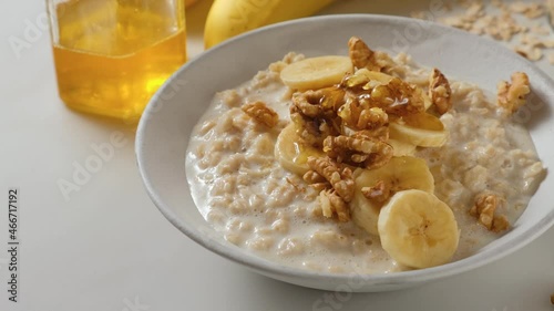 Pouring honey in oatmel porridge with banana, nuts in a plate. Healthy breakfast. Diet food. 4k video photo