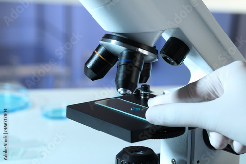 Scientist examining sample of light blue liquid on slide under microscope in laboratory, closeup photo