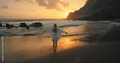 Silhouette pretty woman walks at seaside. Slim female walking along sea water waves on beach at sunset. Travel, vacation, summer concept. Slow motion 4K