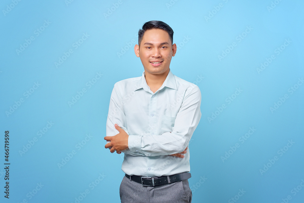 Smiling young handsome businessman crossing hands and look at camera on blue background Smiling young handsome businessman crossing hands and look at camera on blue background
