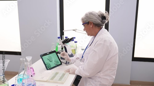 Middle age grey-haired woman wearing scientist uniform using microscope looking embryo image at laboratory photo