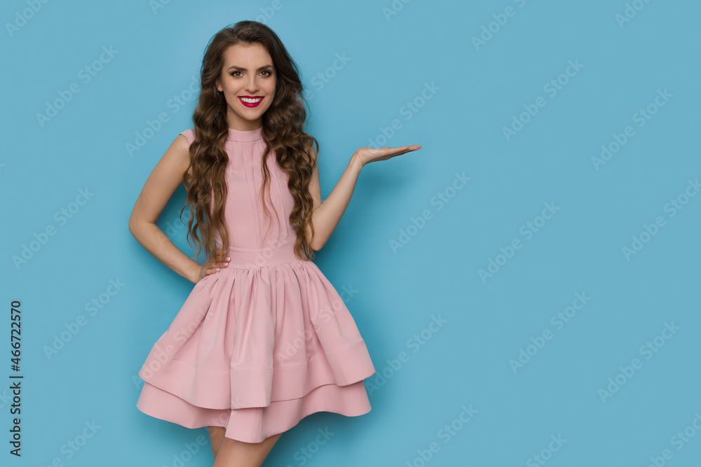 Beautiful young woman in pink cocktail dress is holding hand raised and presenting Beautiful young woman in pink cocktail dress is holding hand raised and presenting