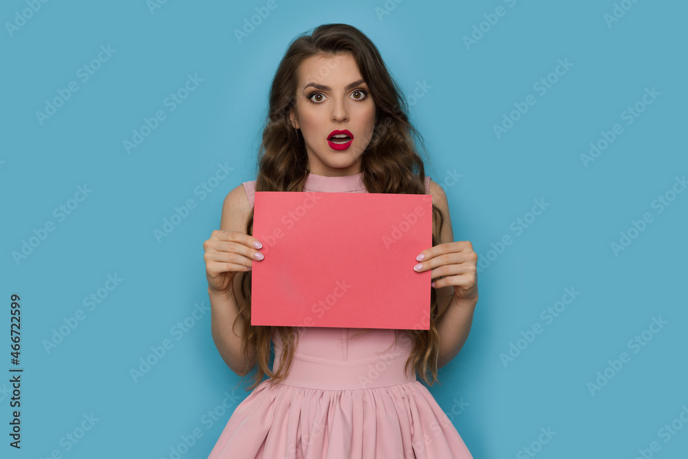 Shocked young woman is holding pink sheet of paper Shocked young woman is holding pink sheet of paper