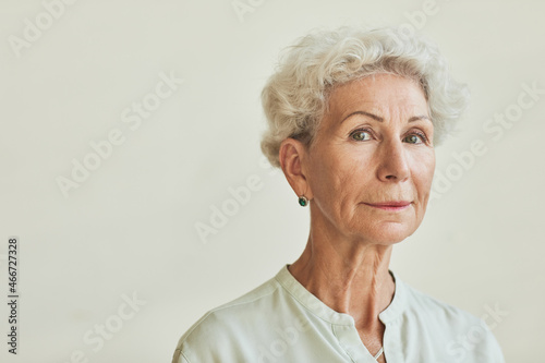 Close up portrait of elegant senior woman looking at camera while standing against neutral background, copy space