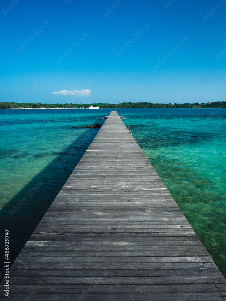 Scenic view of long straight wooden pier over crystal clear turquoise water with coral reef of Koh Kham Island. Near Koh Mak Island, Trat, Thailand.