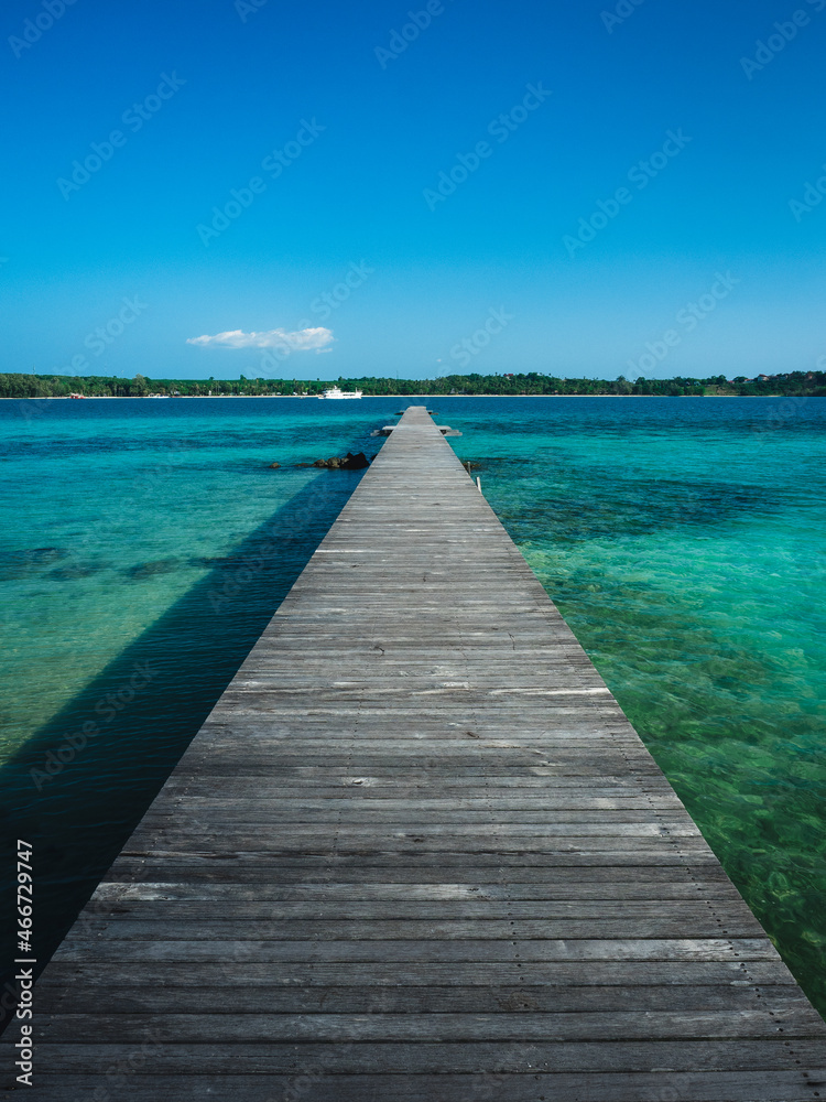 Scenic view of long straight wooden pier over crystal clear turquoise water with coral reef of Koh Kham Island. Near Koh Mak Island, Trat, Thailand. Scenic view of long straight wooden pier over crystal clear turquoise water with coral reef of Koh Kham Island. Near Koh Mak Island, Trat, Thailand.