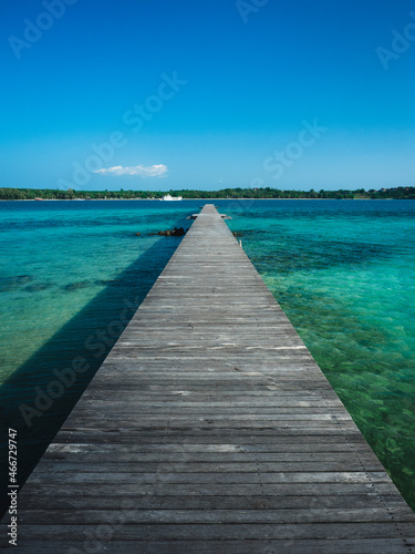 Fototapeta Naklejka Na Ścianę i Meble -  Scenic view of long straight wooden pier over crystal clear turquoise water with coral reef of Koh Kham Island. Near Koh Mak Island, Trat, Thailand.