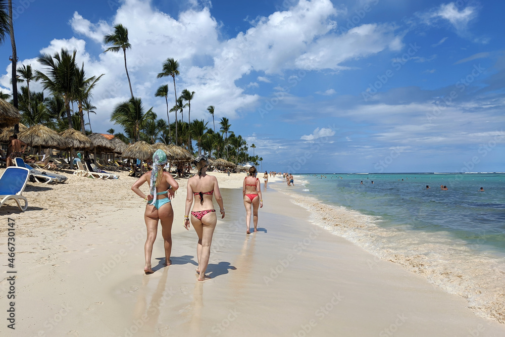 Women in bikini walking by white sand on tropical beach on people and coconut palm trees background. Sea coast, tourist resort on paradise island