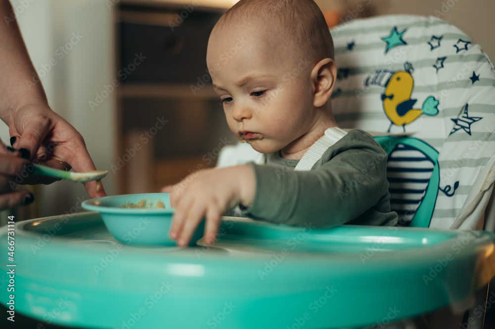 Baby eating with a face stained in food while mother feeds him with a spoon Baby eating with a face stained in food while mother feeds him with a spoon