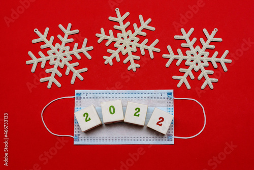 Medical mask with an inscription from cubes 2022 on a red background with snowflakes. Top view with copy space, space for text. Celebrating the New Year. Happy New Year concept.